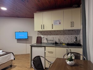 Eine Küchenzeile mit Schränken, einem Fernseher, der 'WELCOME' anzeigt, einem Esstisch mit Stühlen und einer Blumenvase.