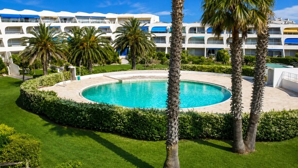 A hotel with a swimming pool surrounded by palm trees and a well-maintained lawn. - Sol-y-Days Jardins du port large terrace and swimming pool (Le Grau-du-Roi)