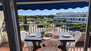A balcony with a table set for two, chairs, a bottle of wine, and a bowl of fruit. - Sol-y-Days Jardins du port large terrace and swimming pool (Le Grau-du-Roi)