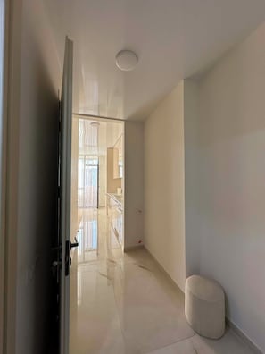 Ein Flur mit Glastür, weißer Wand, kleinem runden Hocker und Deckenleuchte.