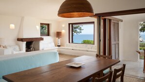 A modern room with a wooden dining table, a sofa, a fireplace, and a view of the sea. - Domus Gallesi by Wonderful Italy (Aglientu)