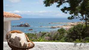 A wicker chair on a balcony overlooking a coastal landscape with rocky shores and a clear sky. - Domus Gallesi by Wonderful Italy (Aglientu)
