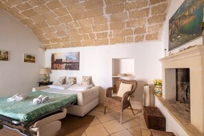 A room with a bed, a chair, a fireplace, and a painting on the wall.