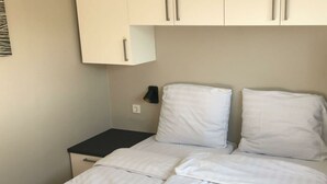 Un lit simple avec une literie blanche, une petite table de chevet et une lampe fixée au mur.
