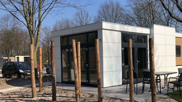 Un bâtiment moderne doté de grandes fenêtres en verre, d’un toit plat et d’un espace extérieur pavé avec une table et des chaises.