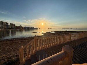 A waterfront promenade with a railing, calm water, and buildings in the background.