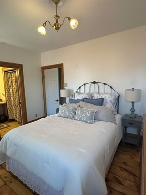 A bedroom with a bed, two bedside tables, a nightstand, a chandelier, and a door.