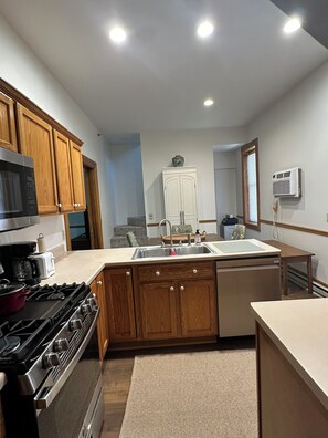 A kitchen with wooden cabinets, a stove, a microwave, a sink, and an air conditioning unit.