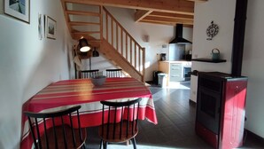 Un comedor con una mesa y sillas, una escalera, una cocina con estufa y una pared decorada con cuadros.