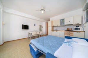 Ein Schlafzimmer mit Bett, Schreibtisch, Stuhl, Fernseher und einer Küchenzeile.
