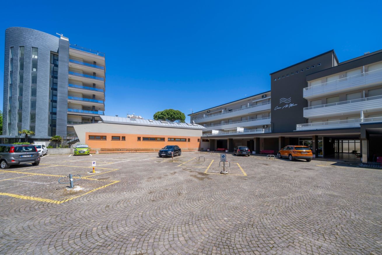 Ein Hotelparkplatz mit Kopfsteinpflasterbelag, mehreren Autos und einem Gebäude im modernen Stil.