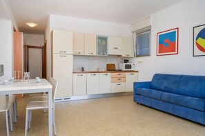 A compact kitchen with white cabinets, a blue sofa, and a dining area with white chairs. - A comfortable and welcoming 61-square-meter apartment, perfect for six people, located on the ground floor (Scala A) of a building directly facing the seafront.The property is situated in Lignano Sabbiadoro in an excellent location, just a two-minute wal (Lignano Sabbiadoro)