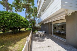 Eine Terrasse mit Tisch und Stühlen, eine Glastür, die zu einem Innenbereich führt, und ein gepflegter Rasen mit Bäumen.