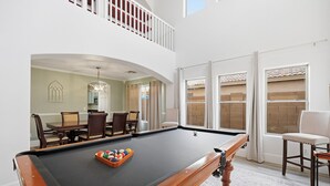 A pool table with a billiard ball rack, a dining area with chairs and a table, and a balcony with a railing. - Marvelous 4-bedroom cottage with billiard room in Casa Grande (Casa Grande)