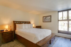 Ein Schlafzimmer mit einem hölzernen Bett, Nachttischlampen, einem Nachttisch, einem kleinen Sessel und einem Fenster mit Aussicht.