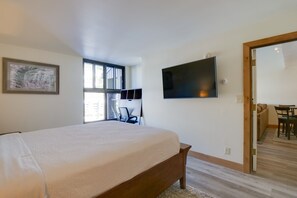 Ein Schlafzimmer mit Bett, einem an der Wand befestigten Fernseher, einem Fenster und einer Tür zu einem Essbereich.