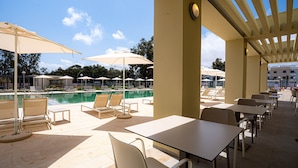 Zona junto a la piscina con sillones, sombrillas y mesas.