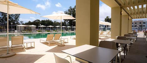 Zona junto a la piscina con sillones, sombrillas y mesas.