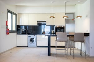 Una cocina moderna con lavadora, hervidor y comedor con sillas.