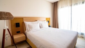 Habitación de hotel con cama, lámpara de noche, mesita de noche y ventana con cortinas.
