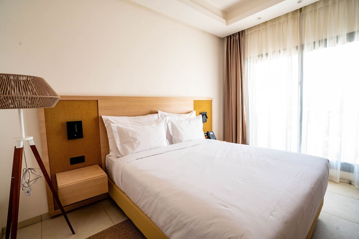 A hotel room with a bed, bedside lamp, nightstand, and a window with curtains.