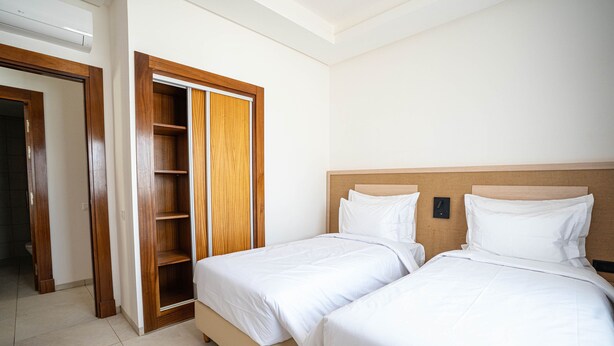 Una habitación de hotel con dos camas, un armario de madera y una estantería empotrada.