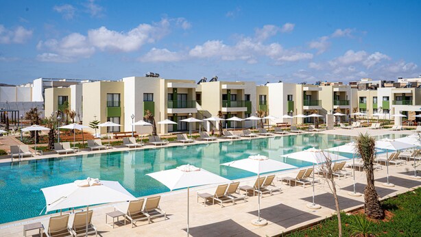 Un hotel con piscina, tumbonas, sombrillas y un cielo azul despejado.