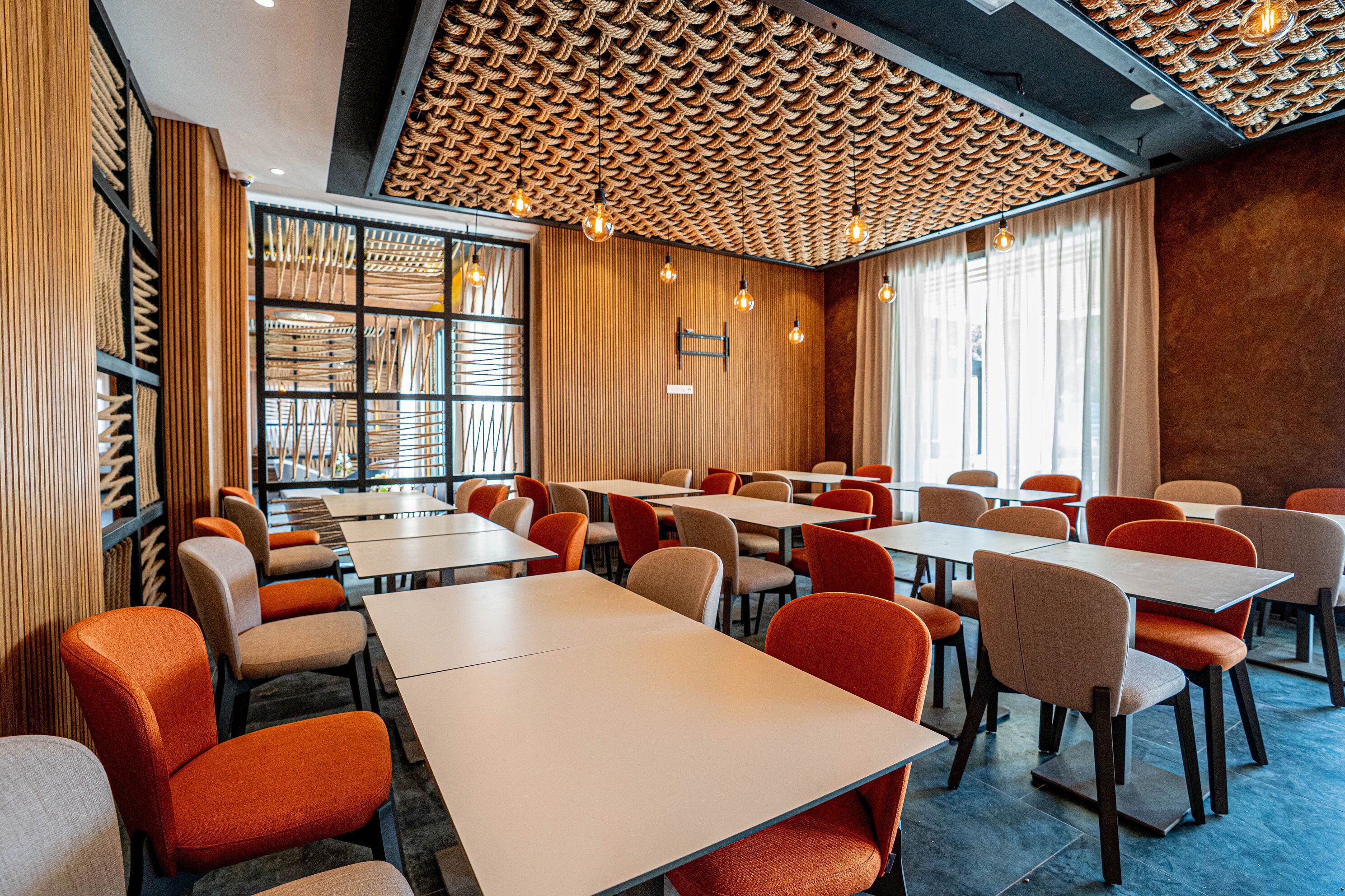 Un comedor moderno con mesas y sillas, un techo con diseño y ventanas amplias.
