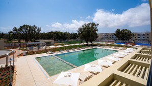 Una piscina con sillas de descanso y sombrillas, rodeada de árboles y edificios.