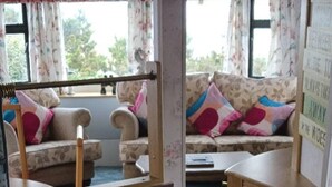A room with a sofa and armchairs, a wooden table, and a window with curtains. - Donegal Mobile Home-coast-family Friendly-sleeps 6 (Gortahork)
