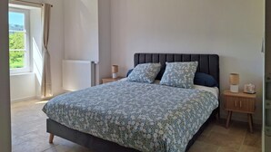 Un dormitorio con cama, mesitas de noche, una ventana con cortinas y una lámpara colgante.