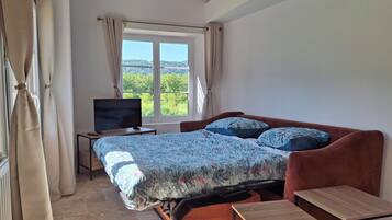 Une chambre à coucher avec un lit, une télévision, une fenêtre avec des rideaux et une vue sur la verdure.