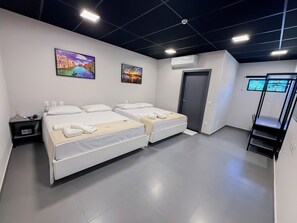 Habitación de hotel con dos camas, un escritorio, una silla, un armario y dos unidades de aire acondicionado fijadas a la pared.