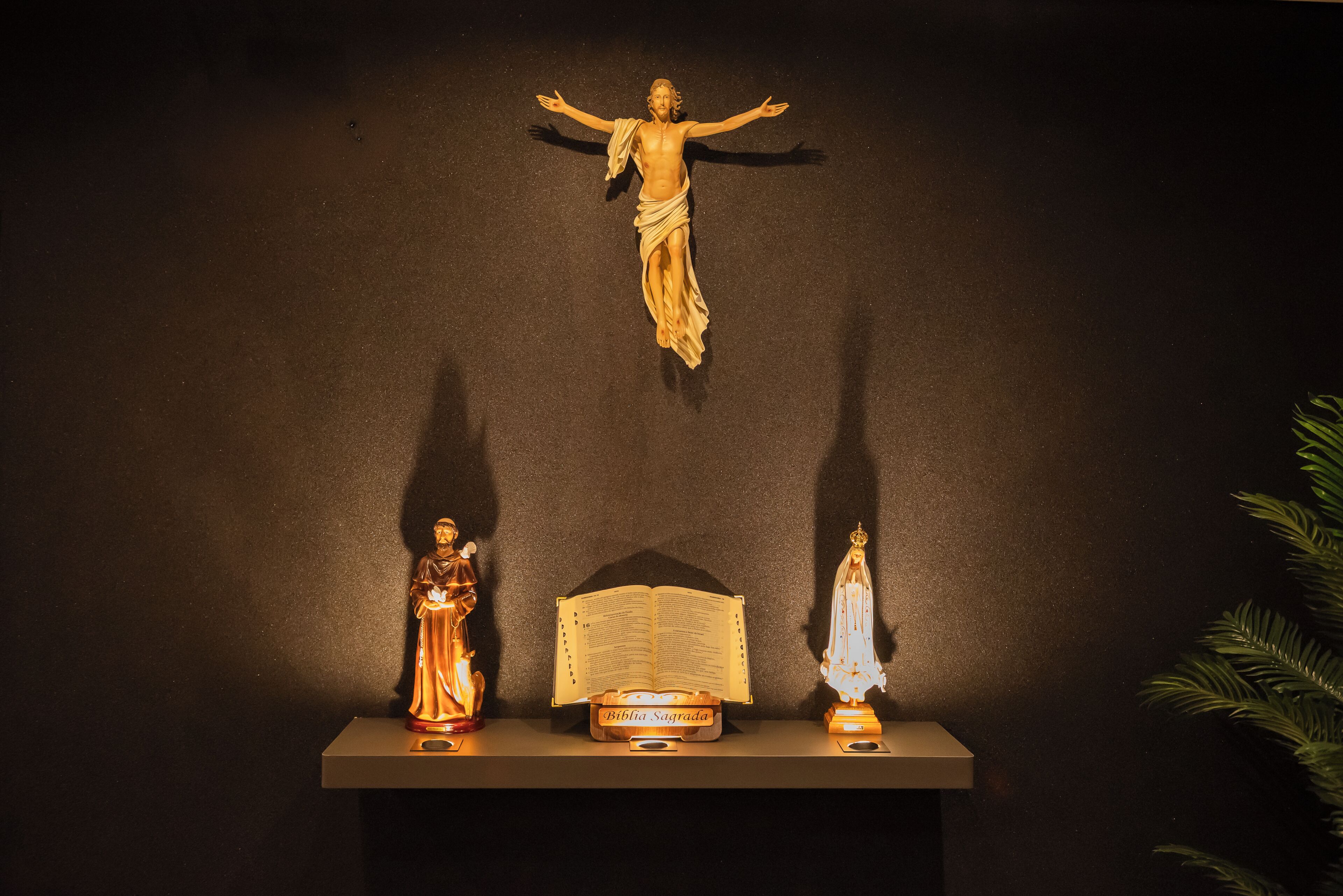 A religious display with a crucifix, a statue, and an open Bible on a shelf.