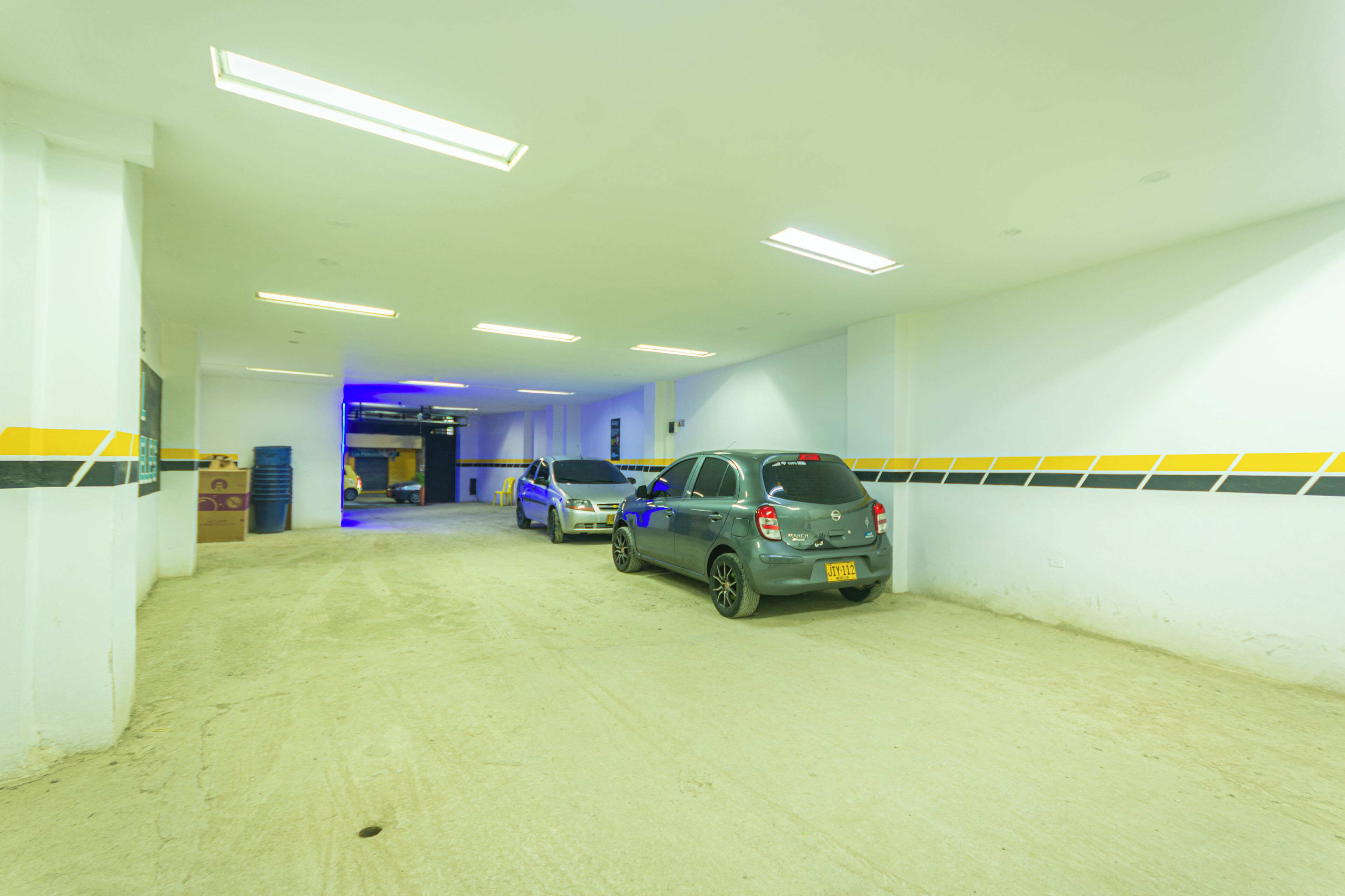 A parking garage with two cars parked, fluorescent lighting, and a yellow and black striped wall.