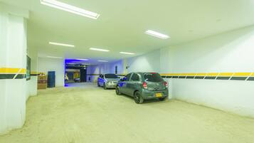 A parking garage with two cars parked, fluorescent lighting, and a yellow and black striped wall.