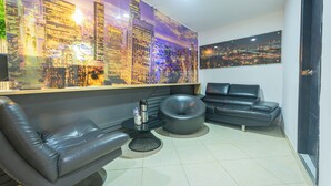 Un salon moderne avec une fresque représentant un paysage urbain, des canapés en cuir, une table basse ronde et un téléviseur à écran plat.