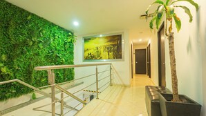 Un espace intérieur moderne agrémenté d’un mur végétal, d’un escalier avec des rampes en métal, d’un grand pot noir contenant un arbre et d’un tableau encadré représentant un paysage urbain accroché au mur.