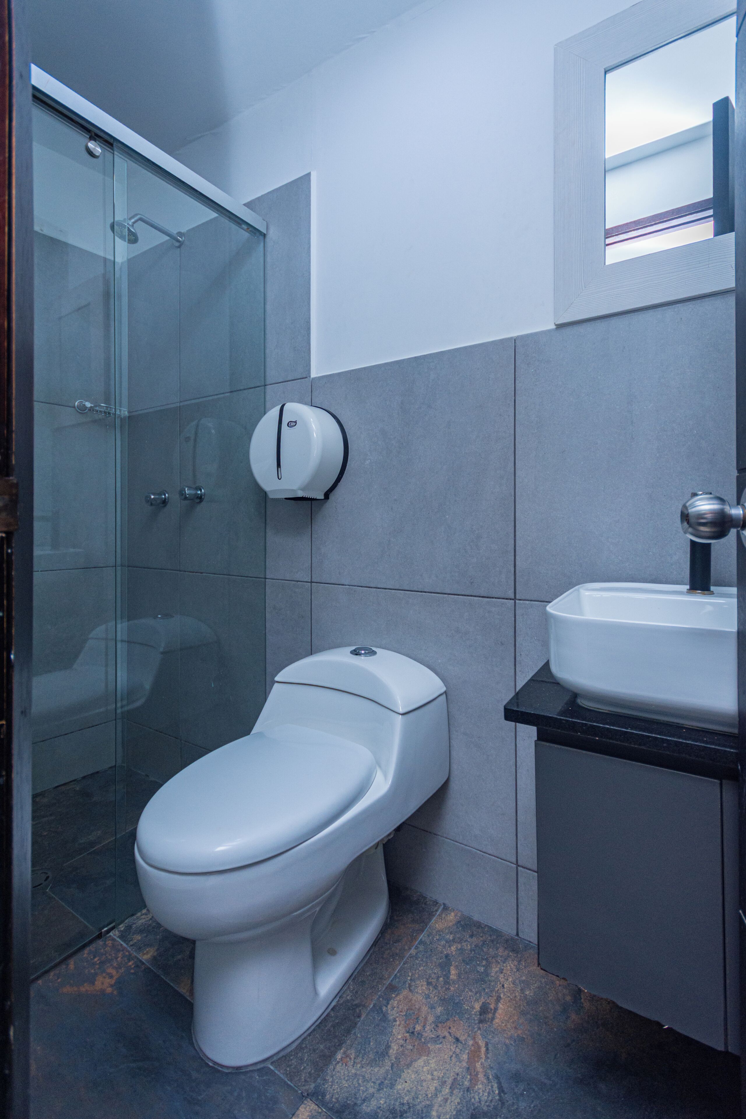 A bathroom with a glass shower enclosure, a white toilet, and a sink with a black countertop.