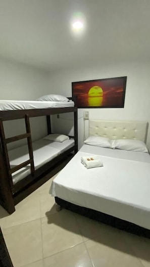 A room with bunk beds, a single bed, a television mounted on the wall, and a white wall.