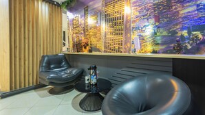 Un espace de détente moderne avec des fauteuils en cuir, une machine à café et une fresque murale représentant un paysage urbain.