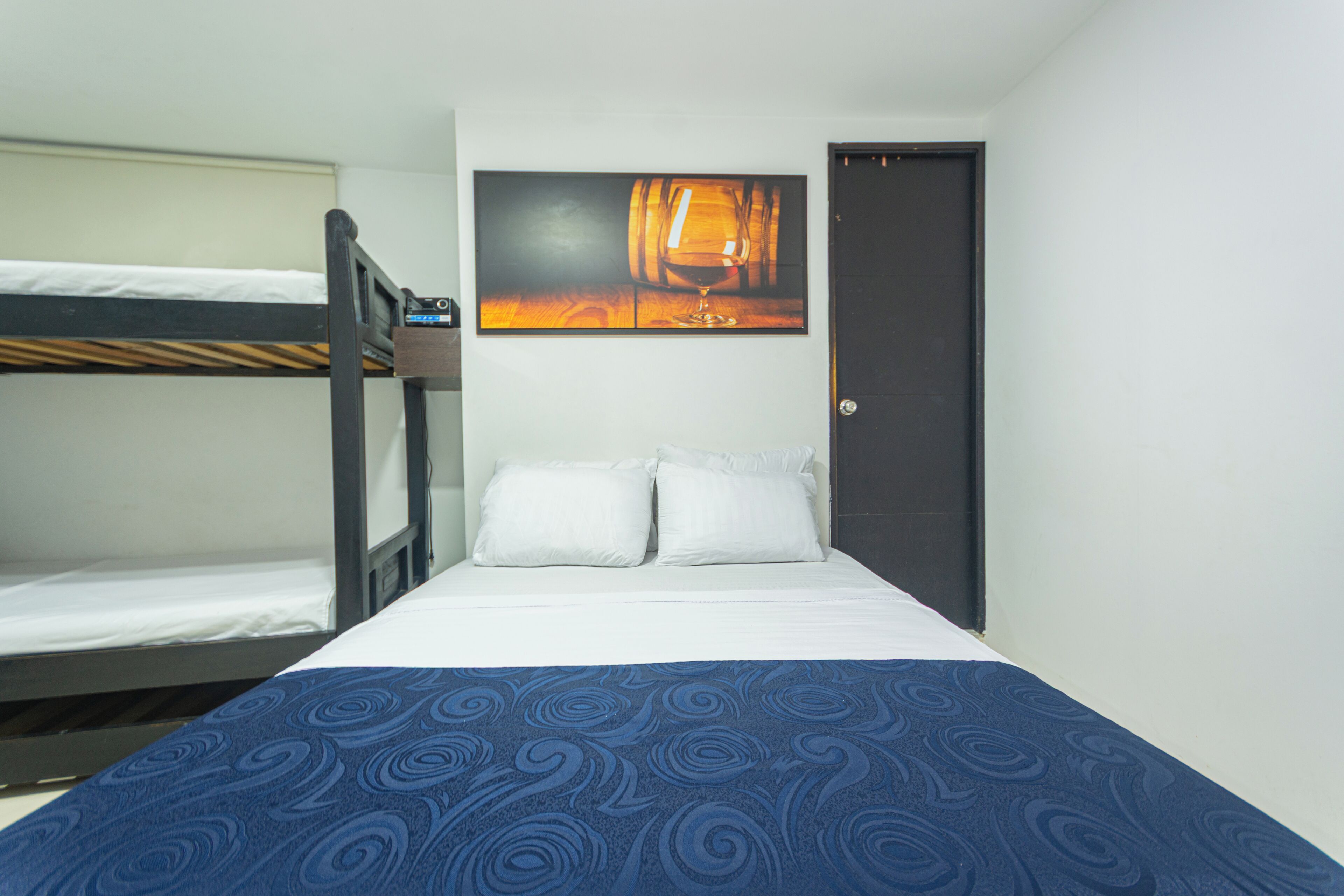 A single bed with a blue patterned bedspread, a bunk bed to the left, and a door with a dark frame.