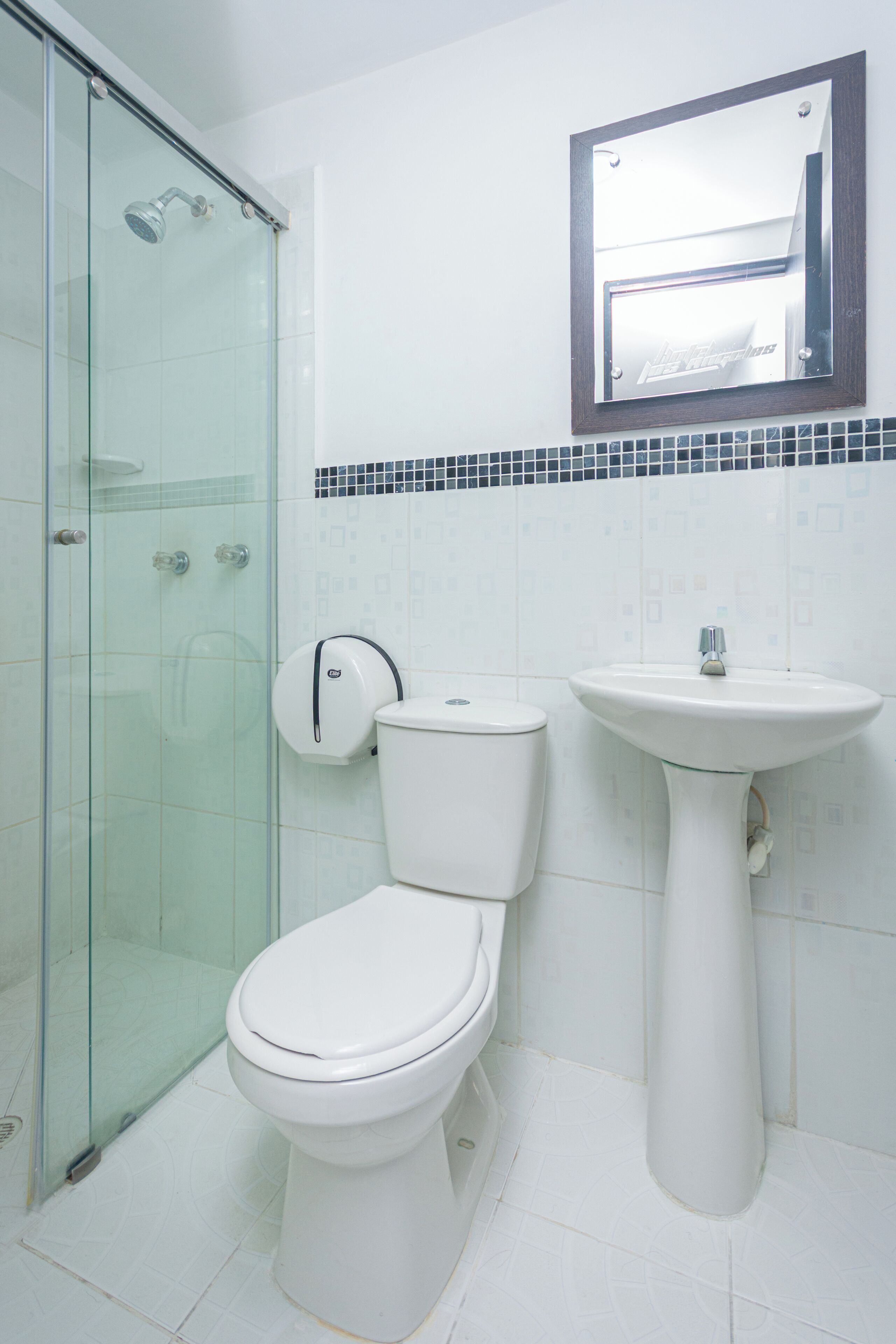 Een badkamer met een douchecabine van glas, een toilet en een wastafel op een zuil.