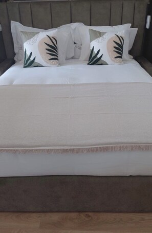 Ein Bett mit weißer Matratze, grauem Kopfteil und dekorativen Kissen mit Blättermotiv.