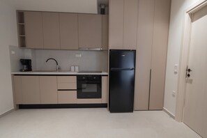 A compact kitchen with a black refrigerator, a built-in oven, and a coffee maker on the countertop. - Marianthi Home by Rentals Pro - Nea Moudania Halkidiki (Nea Moudania)