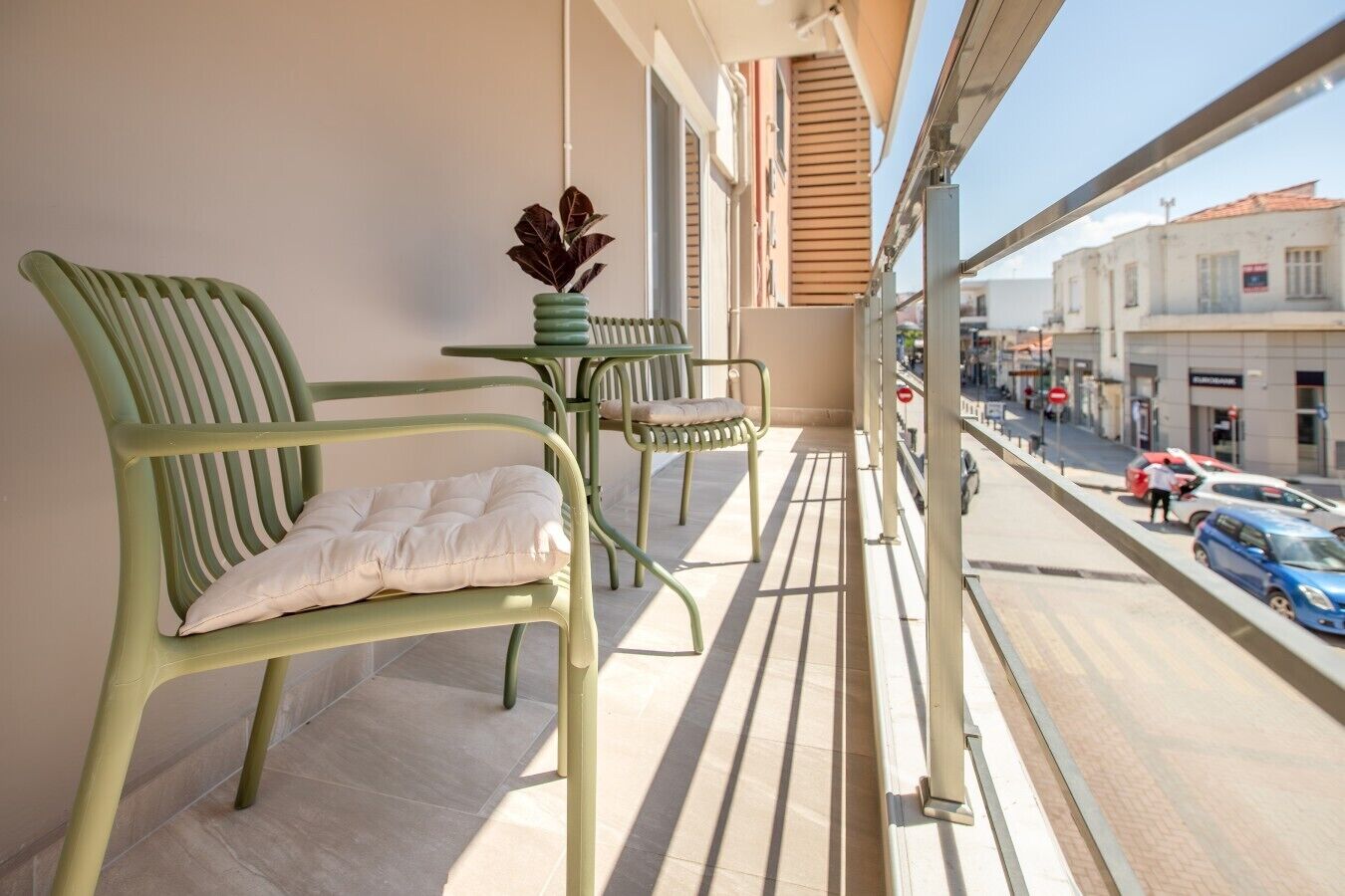 A balcony with two green chairs, a small table, and a potted plant.