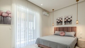 Quarto com cama, mesa de cabeceira, ar condicionado fixado à parede e duas luminárias pendentes.