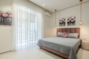 A bedroom with a bed, a bedside table, a wall-mounted air conditioner, and two wall-mounted pendant lights. - Marianthi Home by Rentals Pro - Nea Moudania Halkidiki (Nea Moudania)