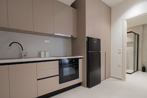 A modern kitchen with a built-in oven, a black refrigerator, and beige cabinetry. - Marianthi Home by Rentals Pro - Nea Moudania Halkidiki (Nea Moudania)