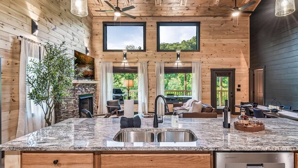 A kitchen with wooden walls, a granite countertop, a double sink, and a dining area with a view of the outdoors. - Wellness & Wilderness - 3b/3.5 bath Family Retreat (Sevierville)
